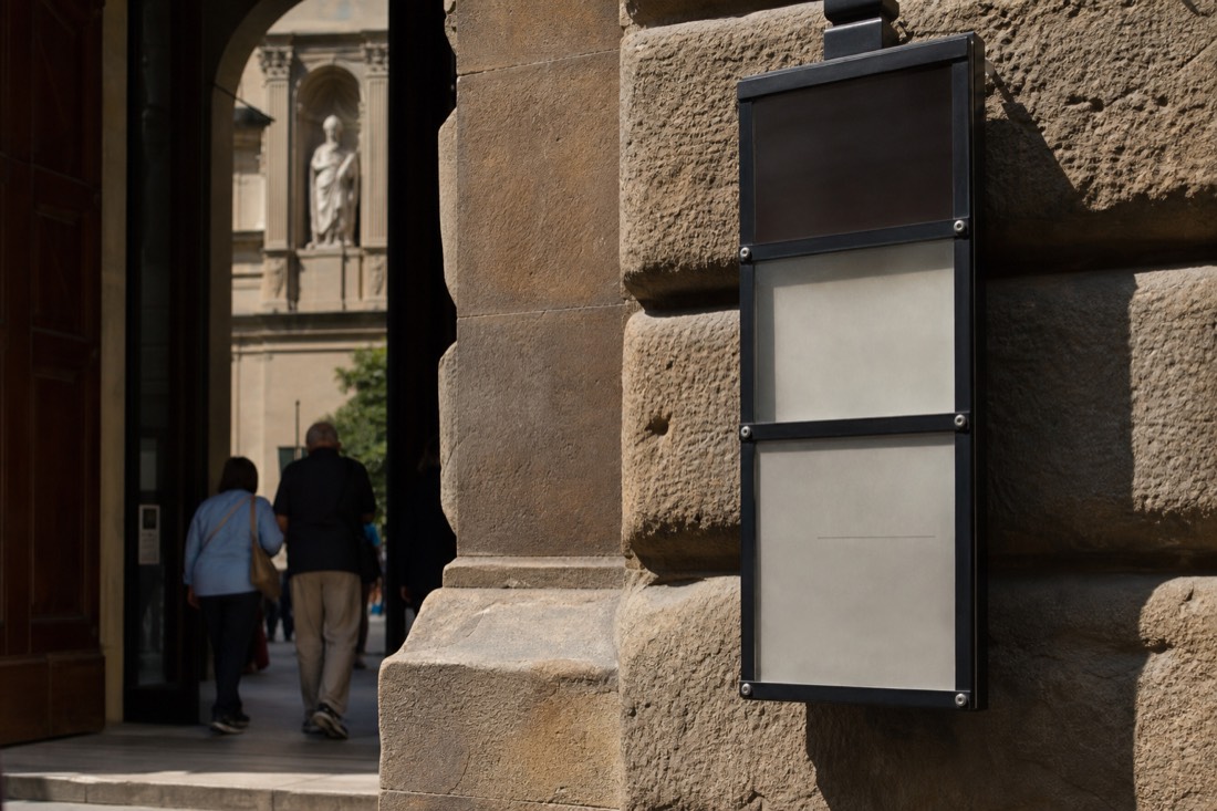 Close-up of the Accademia entrance sign and posted opening hours board on Via Ricasoli in Florence