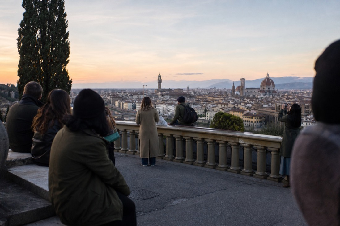 Golden autumn evening light over Florence rooftops seen from the Piazzale Michelangelo terrace with a few people watching the sky